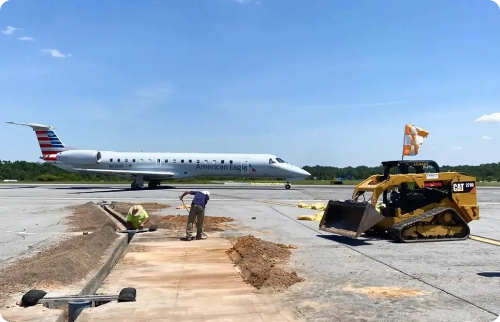 Two commercial electricians dig a trench on airport tarmac to install electrical components
